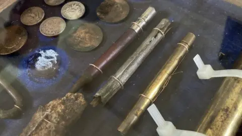 Martin Giles/BBC Display case containing coins and a pencil, among other items found with L/Sgt Charles Stevens
