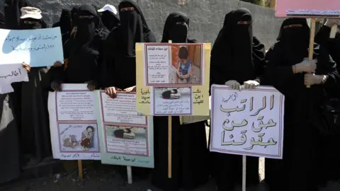 Getty Images Yemeni female teachers and their children attend a protest against the conflict and the suspension of their monthly salaries, outside the UN offices in Sanaa, Yemen