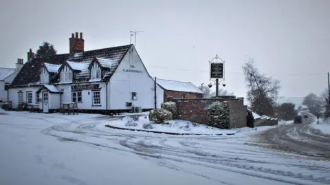 Ian W/BBC Weather Watchers Snow on the road at Hemingby, near Horncastle, with a pub pictured in the background.