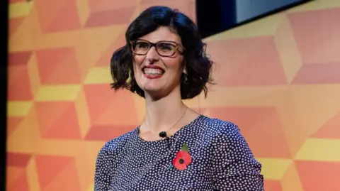 Getty Images Layla Moran is white and wearing a polka-dot blouse. She has short black hair and wears glasses. A poppy is pinned to her top.