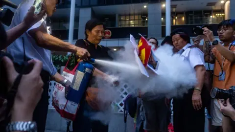 AFP Security guard (L) extinguishes a burning portrait of Chinese leader Xi Jinping held by pro-democracy activist Lui Yuk-lin (2nd L) in Civil Square outside the Central Government Complex after attending a protest march by thousands in Hong Kong on July 1, 2018