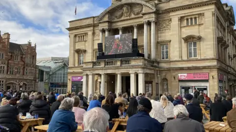 BBC People sitting watching funeral broadcast