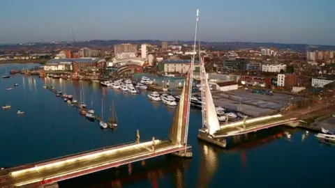 BCP Council Poole's Twin sails bridge in the raised position - lit with gold and red lighting at dusk