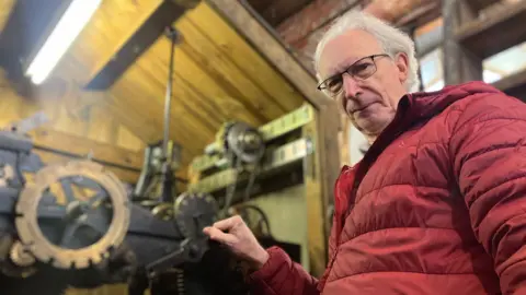 A man in a red puffer jacket stands with the cogs and machinery behind the clock face on St Andrew's Roundhay United Reformed Church.