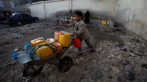 Reuters A boy pushes a wheelbarrow filled with water containers in Sanaa, Yemen (13 October 2017)