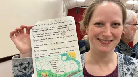 Woman smiling at the camera holding up the letter she had written 