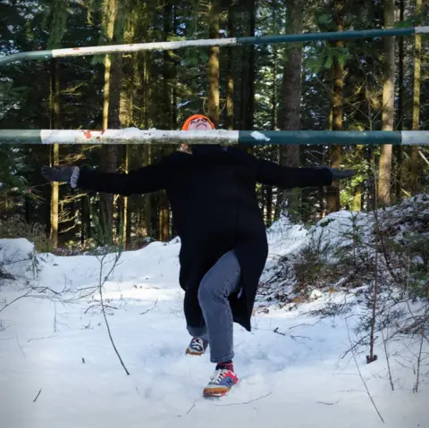 Spei An image of a woman limboing a pole in a snow-covered forest