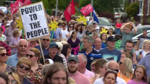 BBC Protesters marching towards Daisy Hill Hospital, with one holding a placard that reads: POWER TO THE PEOPLE