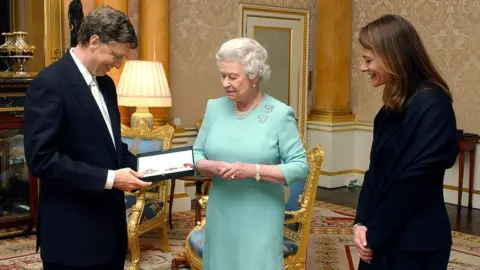 Getty Images Queen Elizabeth II presents Bill Gates with his honorary knighthood at Buckingham Palace, alongside his wife Melinda, in London 2015