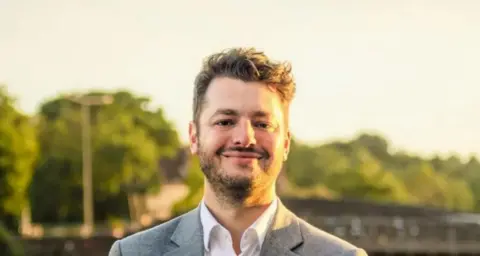 Ipswich Labour Ipswich MP Jack Abbott facing the camera and smiling, with blurred trees in the background