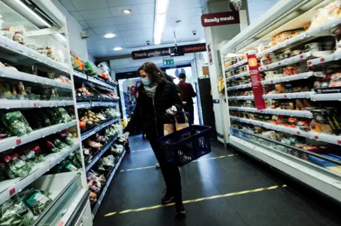 Getty Images Woman in mask examines produce on shelves