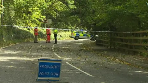 BBC Police officers pictured at a road closed by damage to trees caused by strong winds