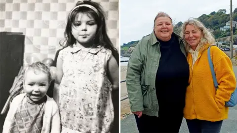 Left: A black‑and‑white photograph of two young girls indoors. The older girl stands wearing a patterned dress with a headband, while a younger girl stands beside her grinning in a checked outfit and cardigan. Behind them is a wall with a distinctive square‑patterned wallpaper and some balloons. Right: A modern colour photograph of two women standing close together outdoors beside the sea. One is wearing a green jacket and dark clothing; the other wears a bright yellow fleece and carries a light blue shoulder bag. Hills, houses, and a coastline appear in the background.