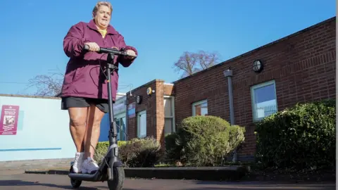 Gemma Laister BBC Cas Evans riding an electric scooter