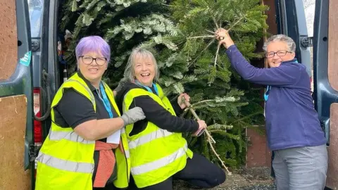 Three women loading Christmas trees into a van