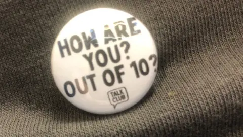 Jon Wright/BBC A small white pin badge with text 'how are You out of 10?'