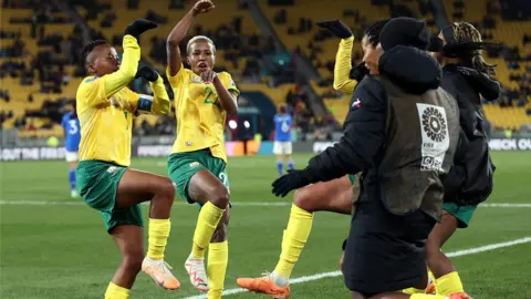 South African players rush to celebrate on the pitch as Thembi Kgatlana strikes a pose after scoring