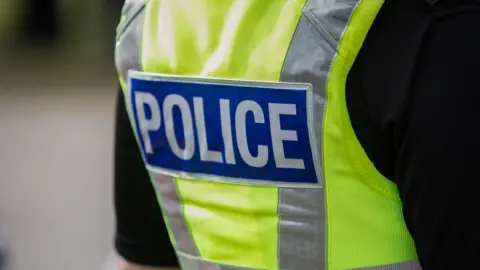 The back of a police officer's uniform, showing a high-vis green jacket with silver stripes, saying 'police' in a blue patch on the jacket.