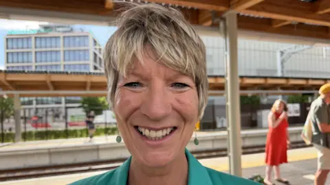 Richard Knights/BBC A close-up of Pippa Heylings. She wears a green top and has green earrings. She is on a station platform.