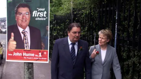 Pacemaker John and Pat Hume pictured beside a John Hume election poster in 1999