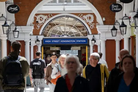 Getty Images Exterior view of High Street Kensington station, with people walking in the foreground