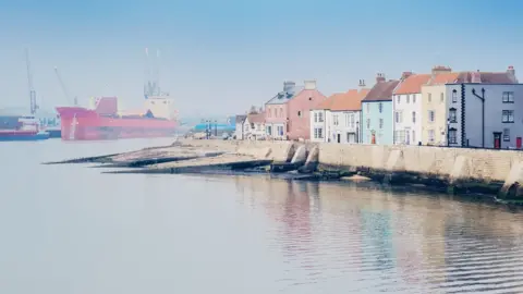 Getty Images Misty view of houses next to sea wall and ship in distance
