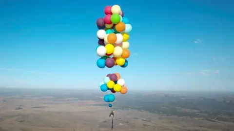 Man in 100 balloons camping chair flight