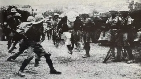 Arthur Lane A black and white photo of rows of soldiers holding batons ready to swing and