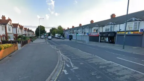 Google view of Grimsby Road with shops on one side of the road and houses on the other. A number of cars and vans can be seen in the distance.