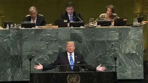 Getty Images Donald Trump addresses the United Nations with outstretched arms in front of a podium emblazoned with the UN emblem