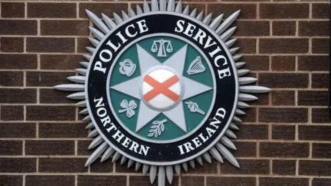 A PSNI crest hangs on a brick wall