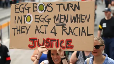 Getty Images A protester in Melbourne holds a placard reading: "Egg Boys turn into egg men when they act 4 racial injustice"