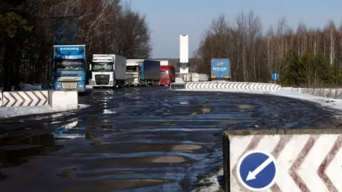 Getty Images Trucks wait to pass Ukrainian border control in front of the Three Sisters monument at the border crossing between Ukraine, Russia and Belarus on 14 February 2022 in Senkivka, Ukraine