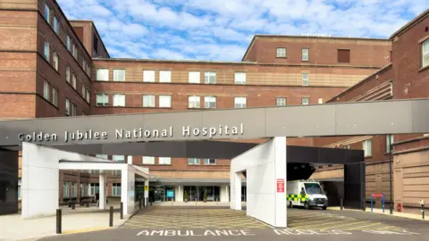 Getty Images Exterior of Golden Jubilee National Hospital. An ambulance is parked outside a modern five-storey building. 