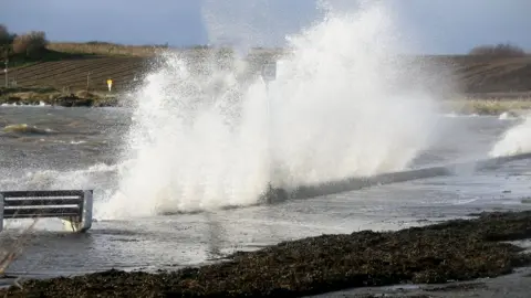 Stephen Davison A wave is crashing on a harbour wall creating a large splash over the wall.