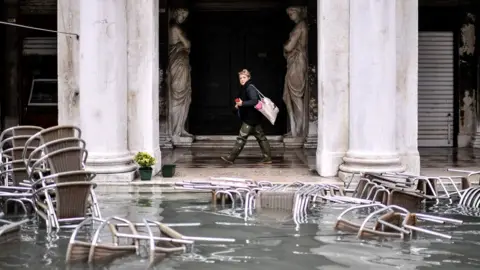 Getty Images A woman walks past flooded furniture of a cafe terrace as Venice suffers in extremely high water levels, 13 November 2019