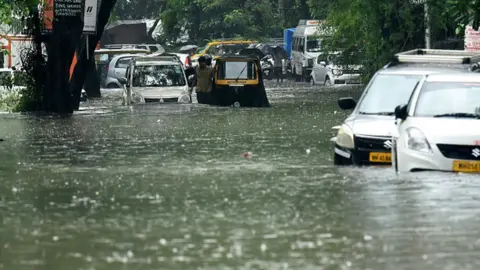 Getty Images Vehicles drive through a flooded street during rain showers in Mumbai on July 5, 2022