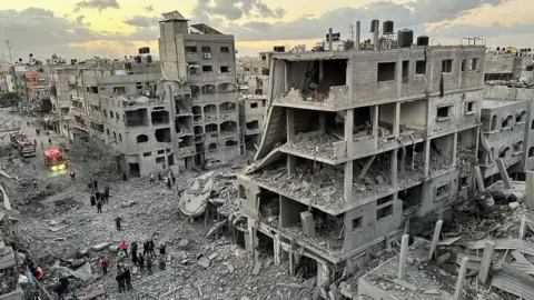 Reuters Palestinians walk past destroyed buildings in Jabalia refugee camp, in the north of the Gaza Strip (21 November 2023)