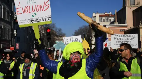 AFP A protester wearing yellow vest (gilet jaune) holds a baguette and a sign reading "Citizens Referendum Initiative in Marseille, 15 December