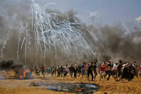 MOHAMMED ABED/afp Palestinians run for cover from tear gas during clashes with Israeli security forces near the border between Israel and the Gaza Strip, east of Jabalia on 14 May 2018.