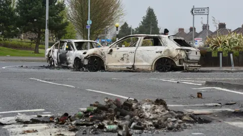 Pacemaker Burnt out cars remain on the road on 4 April following violence in Newtownabbey the night before