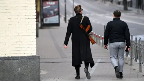 DANIEL LEAL/AFP A man carrying a Kalashnikov AK-47 rifle walks in central Kyiv on February 25, 2022