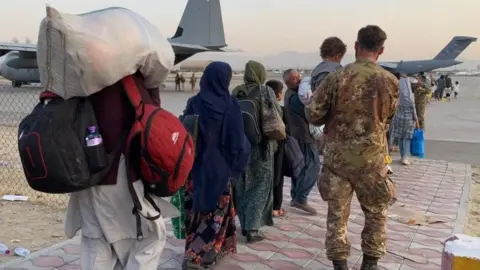 BBC People walking towards planes waiting at Kabul airport