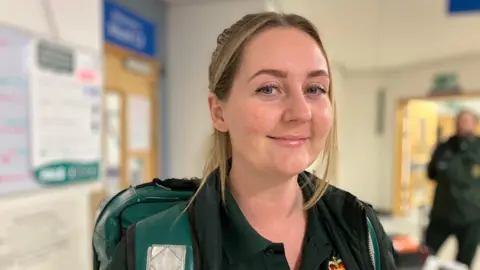 Paramedic Rebecca Baldwin stands in a hospital corridor wearing her uniform.