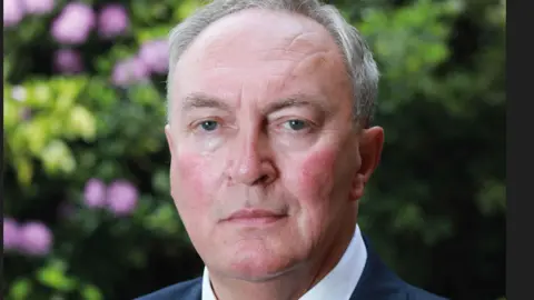 USDAW A white man with grey hair stares at the camera. He is wearing a blue suit jacket, white shirt and red tie.