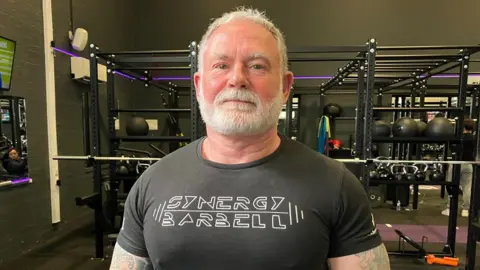 Paul Collinson standing in front of gym equipment, mainly weights.