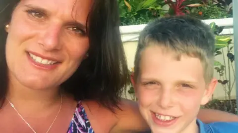 Family handout A woman with dark brown hair and a silver necklace is hugging her son, a young boy with brown hair who is smiling. 