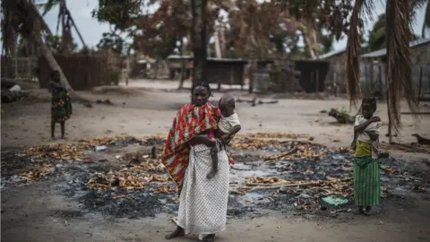 AFP A woman holds her younger child while standing in a burned out area after an on the village of Aldeia da Paz outside Macomia, Mozambique - 24 August 2019