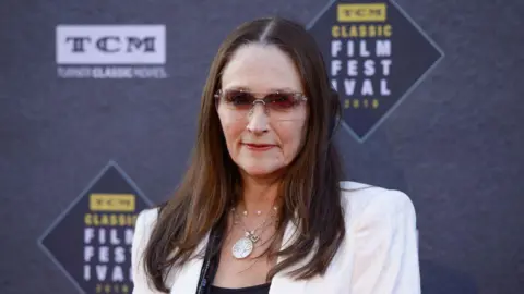 Olivia Hussey wears sunglasses and a white blazer on the red carpet of the TCM Classic Film Festival in 2018