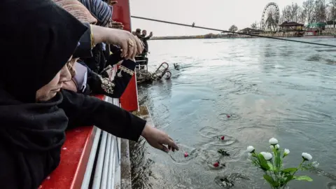 AFP Iraqi women throw flowers into the River Tigris in Mosul in remembrance of those killed in a ferry accident (22 March 2019)